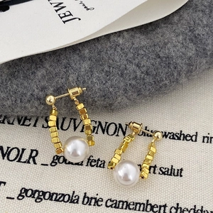 Détail de boucles d'oreilles dorées en U avec perles carrées et une perle blanche
