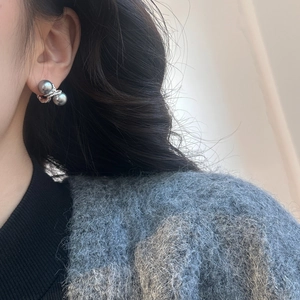 Detail of twisted metal stud earrings with grey pearls on a model in profile view