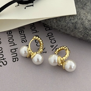 Detail of twisted gold earrings with double pearls on grey textured surface