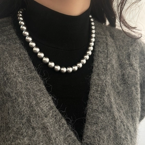 Élégant collier de perles gris argenté porté par un mannequin sur un col roulé noir