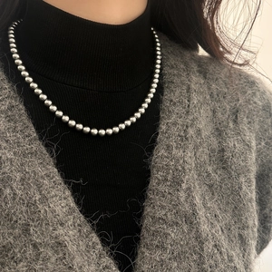 Gros plan d'un collier de perles en métal argenté sur un pull noir élégant