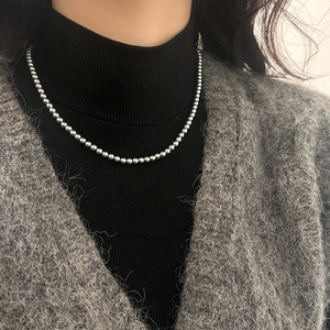 Gros plan d'un collier de perles argentées minimaliste porté sur un pull à col roulé