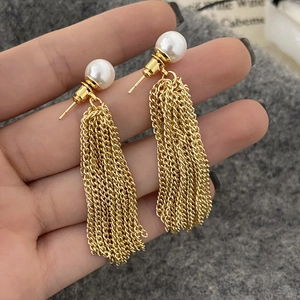 Detail of long gold tassel earrings with grey pearls and fine chains held in hand