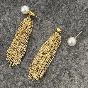 Macro shot of long golden tassel earrings with white pearls on a grey background