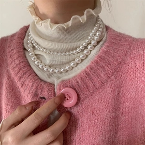 Gros plan d'un collier de perles blanches double rang élégant sur un pull en maille rose