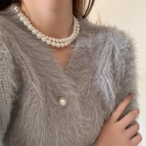 Gros plan d'un collier de perles blanches double épaisseur avec cardigan gris duveteux