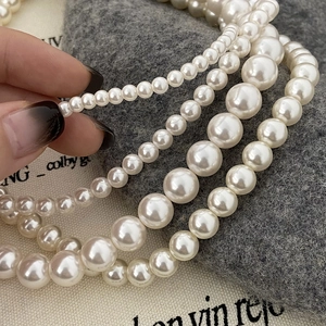Vue détaillée de plusieurs tailles de colliers de perles blanches superposés sur tissu