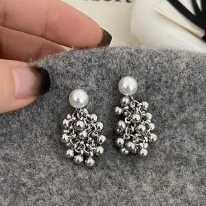 Close-up of pearl stud earrings with silver metal bead fringe details on hand