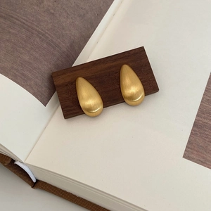 Détail de boucles d'oreilles goutte d'or mat avec texture en métal brossé sur bois