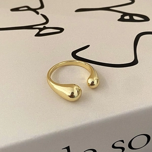 Close-up of minimalist gold crossover ring with teardrop ends on a textured book page