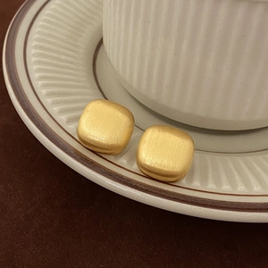 Macro shot of gold square matte brushed earrings on a textured ceramic dish