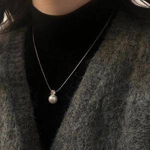 Elegant gold pearl pendant necklace with zircon accent worn over a black sweater