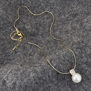 Detail of gold pearl pendant necklace with zircon accent on a dark grey textured background