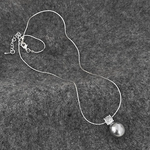 Macro detail of silver necklace with gray pearl and sparkling zircon pendant on felt