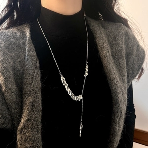 Detail of silver leaf tassel necklace layered on a dark turtleneck for a chic look