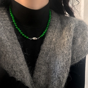 Collier de perles en pierre naturelle vert foncé avec fermoir argenté sur veste grise