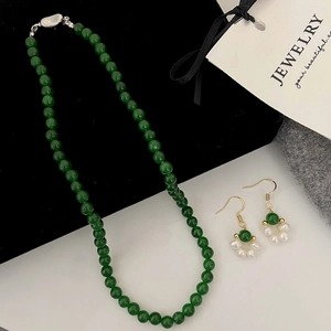 Vue détaillée du collier de perles vert émeraude et boucles d'oreilles sur velours