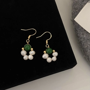 Détail de boucles d'oreilles dorées avec perles vert émeraude et perles baroques sur velours