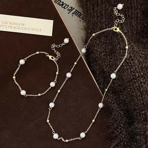 Detail of freshwater pearl necklace and bracelet set with gold chain on warm texture