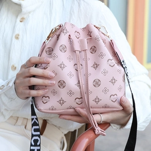 Pink monogram drawstring bucket bag with a wide lettered strap on a white textured shirt
