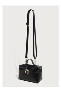 Detail of black glossy leather box bag with dual gold zippers and detachable strap