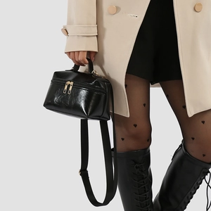 Glossy black leather box bag with gold zippers and wide strap shown on a model