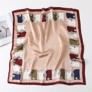 Gros plan d'un foulard carré en soie champagne et bordeaux aux motifs géométriques élégants
