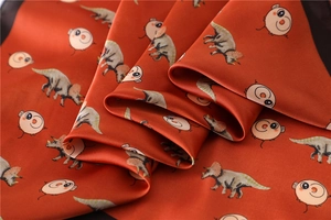 Detailed view of silk-like neck scarf featuring cute cartoon dinosaur and pig prints