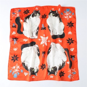 Detail van zijden vierkante sjaal met kattenpatronen en bloemmotieven op oranje basis