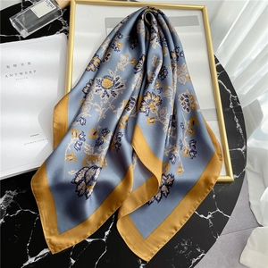 Elegant floral silk scarf in mist blue and gold displayed on a marble surface