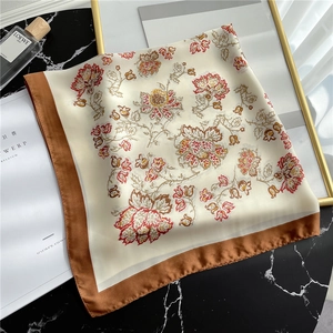 Detailed macro view of vintage floral square silk scarf with brown border on marble surface