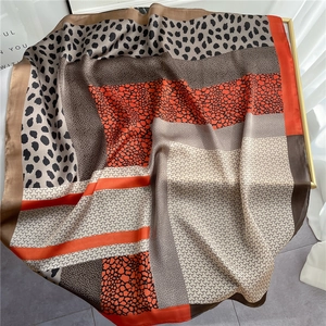 Leopard print silk scarf with orange and brown patchwork patterns on a gold stand