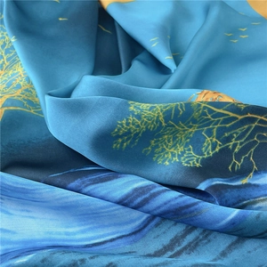 Detailopname van een zijden vierkante sjaal met blauwe motieven en gouden bomen
