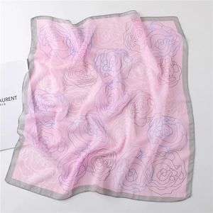 Detailed view of pink chiffon square scarf with blue abstract rose patterns and gray hem
