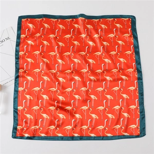 Detailed flat lay of a square silk scarf with red flamingo pattern and green borders