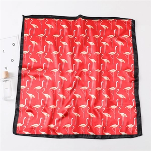 Detailed flat lay of a red satin square scarf with flamingo prints and black silk borders
