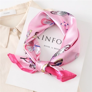 Pink butterfly print silk scarf tied in a bow on a white book for summer styling