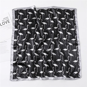 Detail of satin silk square scarf featuring elegant white flamingo patterns on black fabric