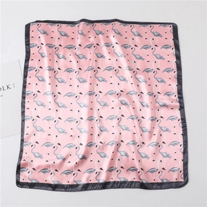 Flat lay of pink silk scarf with flamingo print and grey edges next to a magazine