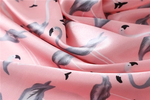 Close-up of pink silk scarf fabric featuring elegant flamingo patterns and satin texture