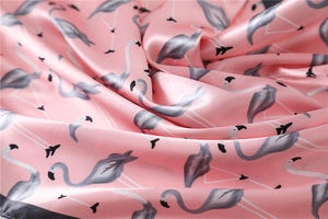 Detail of pink satin scarf fabric featuring elegant repeating flamingo prints and glossy texture