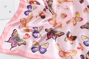 Detailed close-up of pink silk scarf featuring colorful butterfly prints and smooth texture