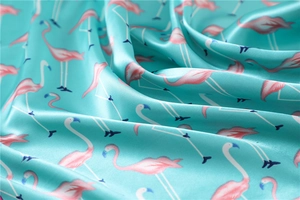 Macro detail of glossy teal silk scarf featuring decorative pink flamingo print patterns