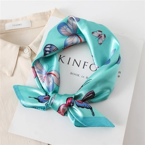 Detail of mint green silk scarf with butterfly print tied in a bow on a white shirt