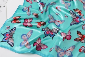 Detail of silk-like scarf featuring colorful butterfly patterns on a bright teal satin fabric