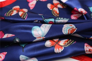 Macro shot of smooth dark blue satin scarf fabric with vibrant colorful butterfly patterns