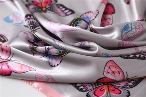 Detail of silk scarf showing vibrant butterfly print and smooth satin texture on silver grey