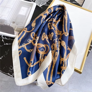 Detail eines Seidenquadrats in Marineblau mit Goldketten und Reitsport-Print auf Marmor
