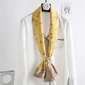 Elegant narrow yellow silk scarf with floral print tied on a white shirt background