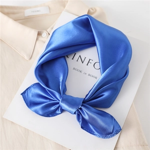 Elegant bright blue satin square scarf tied in a bow on a beige shirt background